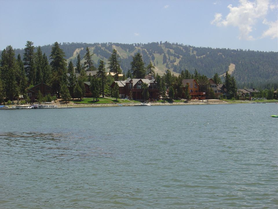 Lakefront with houses and trees, ski slope on mountain.