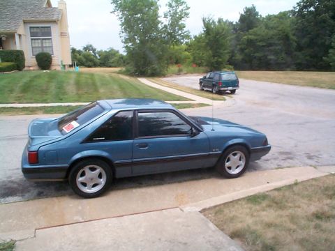 1987 Ford Mustang - Blue 1987 Ford Mustang coupe parked on a suburban driveway next to a house.