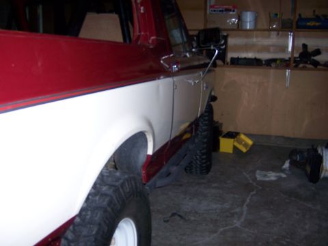1991 Ford Bronco - Side view of a two-tone red and white pickup truck with off-road tires, parked indoors.