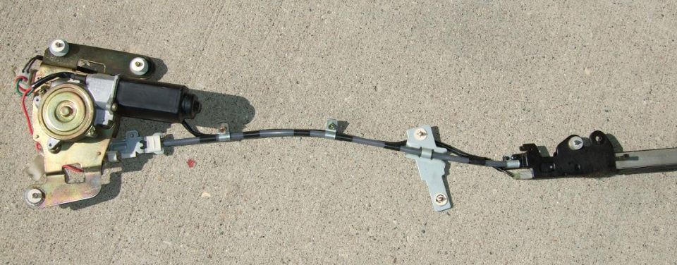Power window regulator assembly with motor, cable, and mounting brackets on concrete