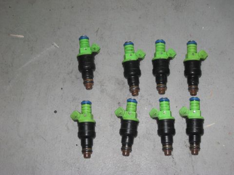 1991 Ford Bronco - A set of eight fuel injectors, each with green tops and black bodies, are laid out on a concrete surface.