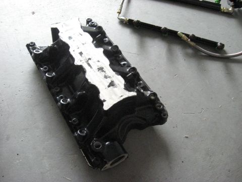 1991 Ford Bronco - A black intake manifold with a fuel rail assembly sits on a gray concrete surface.