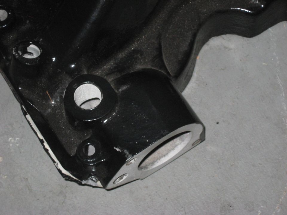 Black metal automotive part with circular openings and mounting holes, resting on a gray surface