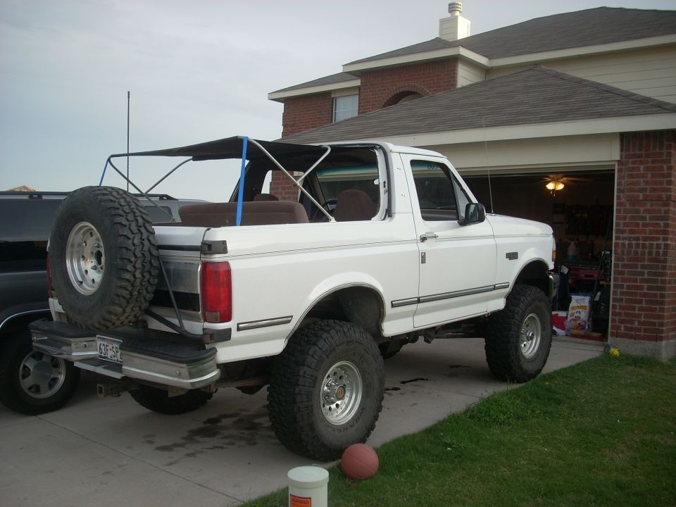 White 1992 Ford Bronco with a soft top, spare tire, and lifted suspension parked in a driveway