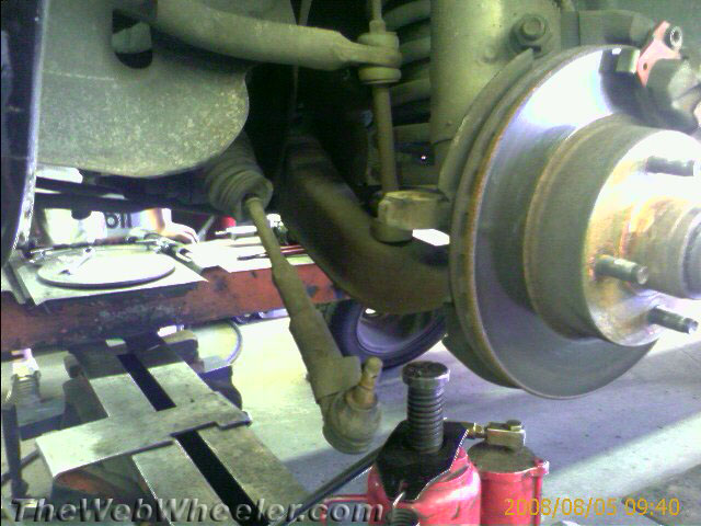 Close-up of a car's front suspension components, including a brake rotor and tie rod end