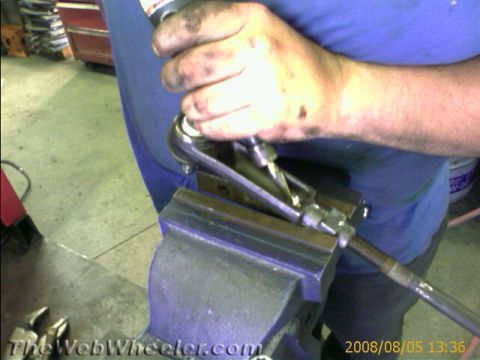 1985 Ford Mustang - A mechanic works on a suspension component held firmly in a vise, using a ratchet wrench.