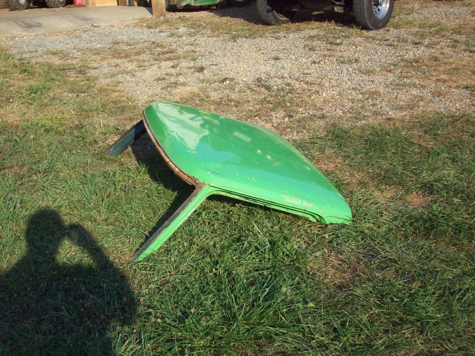 green hardtop sitting on grass, part of a vehicle in background