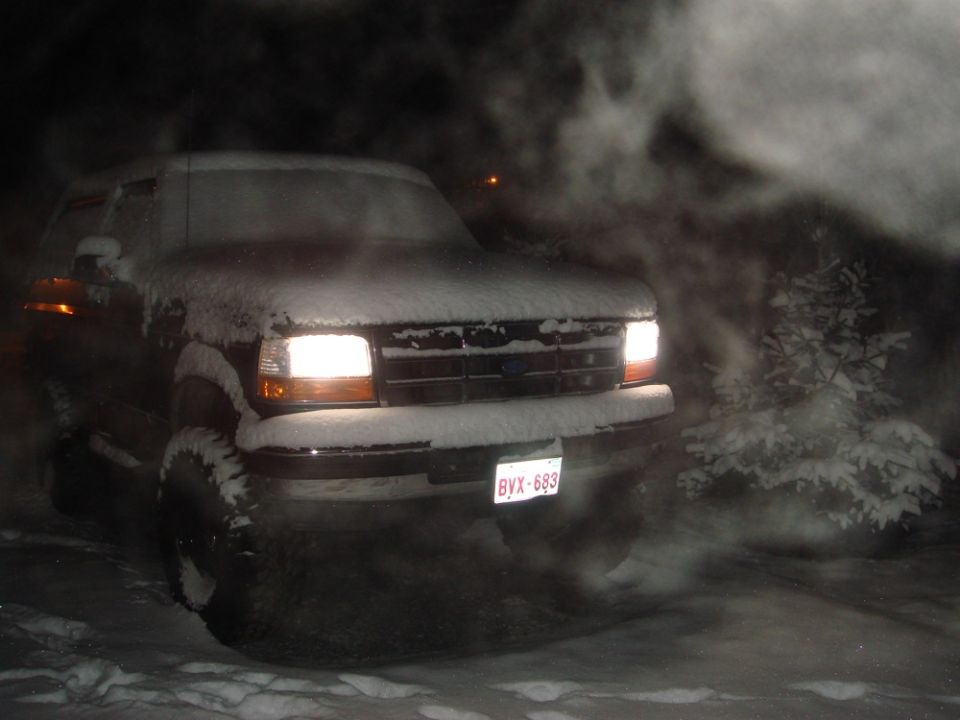 Ford truck with snow on it, headlights on, in a snowy area at night. License plate BYX-683 visible