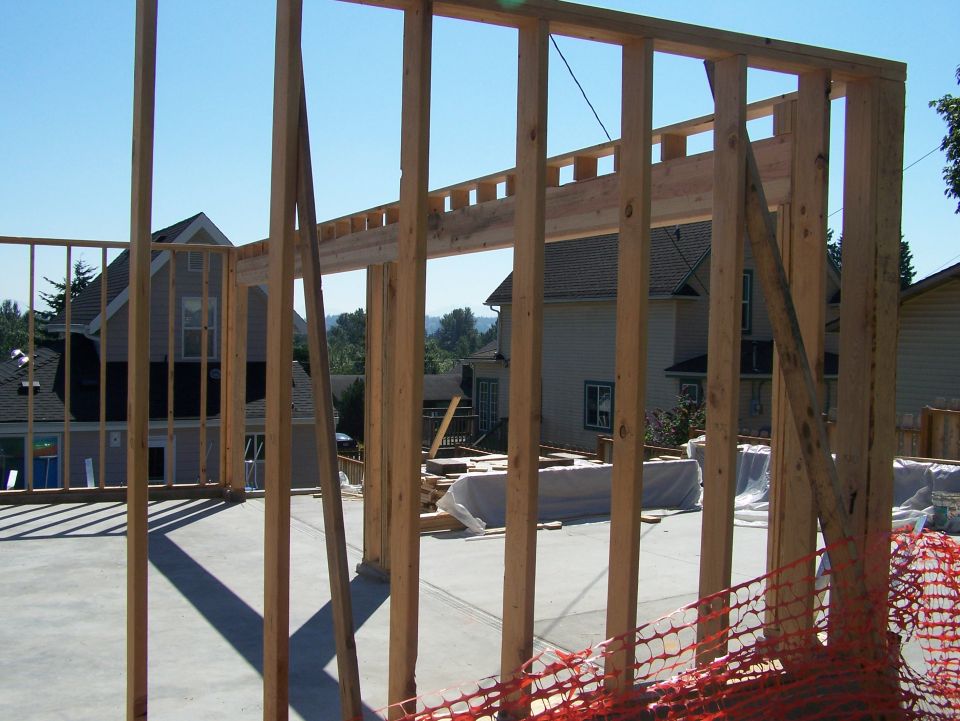 Building construction framing with houses in the background.