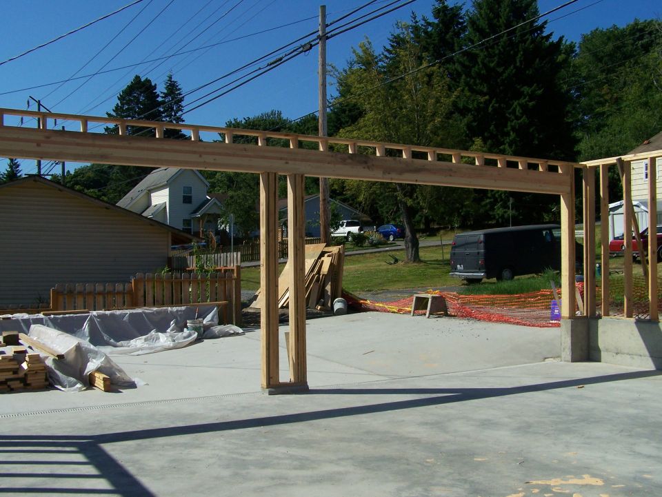 Construction site with wooden framing for a new building, concrete floor, and background houses and trees.