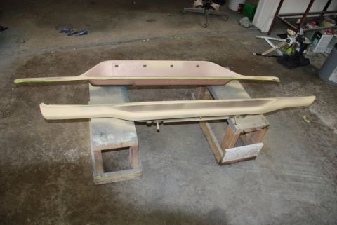1996 Ford Bronco - Photograph of two primed body trim panels on wooden stands in a shop, not a document.