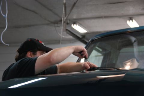 1996 Ford Bronco - Photograph of a person working on the windshield area of a green vehicle inside a shop.