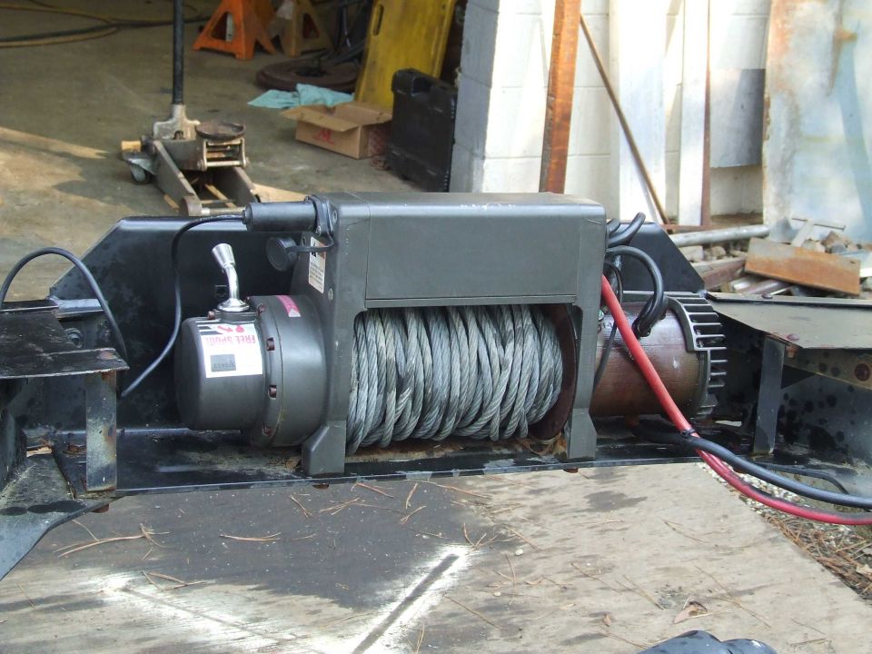 Winch mounted on a black metal frame, with a coiled steel cable and red and black wires