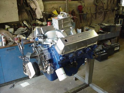 1979 Ford Bronco - A Ford Motorsport engine with blue block and silver valve covers is displayed on a stand in a workshop.