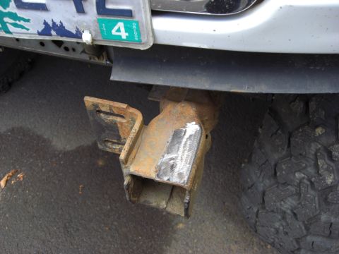 1993 Ford Bronco - Close-up of a rusty trailer hitch receiver, showing weld repairs and a portion of a tire.