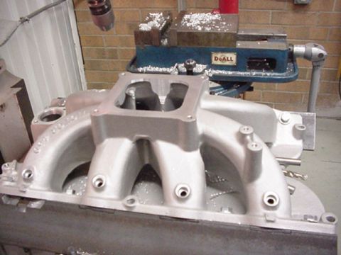 1979 Ford Bronco - An aluminum intake manifold is shown in a workshop setting, with a milling machine visible in the background.