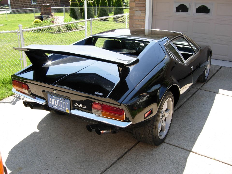 Black DeTomaso Pantera rear view with wing and Michigan 4NXOTIC plate in a driveway