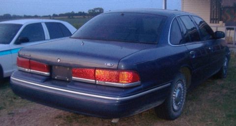 1997 Ford Crown Victoria - A dark blue sedan is parked next to a white vehicle with blue stripes.