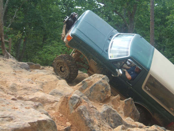 Green and tan Bronco tilted on a steep rock climb with front tire in the air