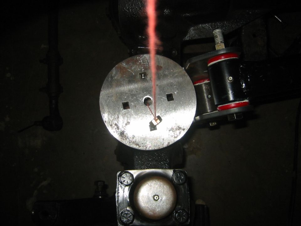 Close-up of a metal disc with a red fluid stream going through it, attached to black suspension parts