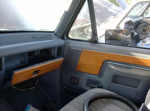 1989 Ford Bronco - The interior of a vehicle shows wood trim and an open glove box, with another vehicle visible outside.