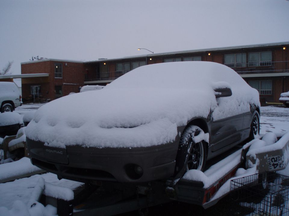 Snow-covered Pontiac coupe on a trailer in front of a brick motel