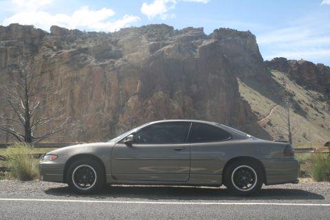 2002 Pontiac Grand Prix - A gray 2002 Pontiac Grand Prix is parked on the side of the road with a large rock formation in the background.
