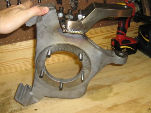 1986 Ford Bronco - A close-up shows a modified steering knuckle with a welded bracket and bolts, with a hand holding it.