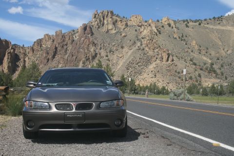 2002 Pontiac Grand Prix - A gray 2002 Pontiac Grand Prix is parked on the side of a road with a scenic mountain backdrop.