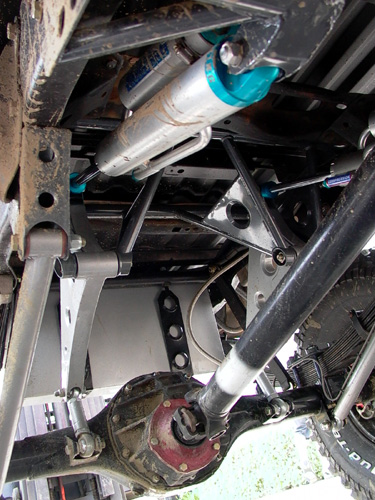 1984 Ford Bronco - Underbody view looking up at a lifted truck's rear suspension, showing a solid axle housing with a red differential, leaf spring pack, blac…