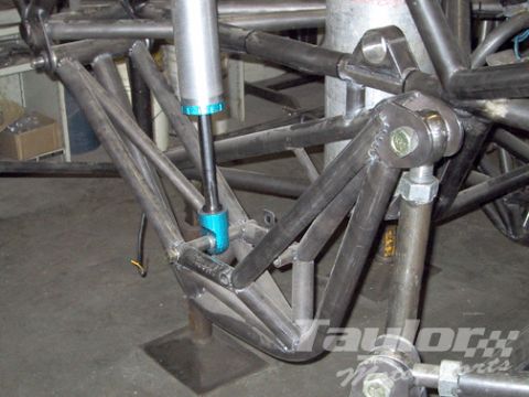 1984 Ford Bronco - Close-up of a bare-steel tube-chassis rear suspension under construction, with triangulated round-tube links, a fabricated trailing arm and…