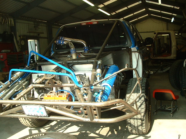 Black prerunner truck with tube rear chassis, blue coilovers and bypass shocks in a shop
