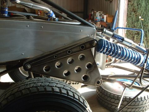 1984 Ford Bronco - Close-up of a fabricated cantilever rear suspension on a tube-chassis off-road buggy in a shop, showing a lightening-holed steel rocker pla…