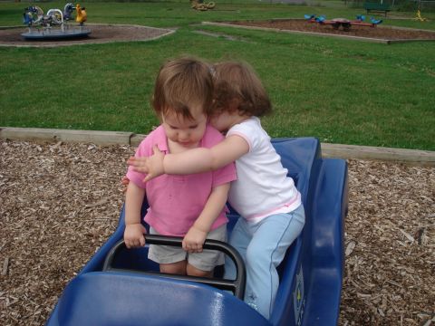 2000 Ford Crown Victoria - Two young children share a moment in a blue toy car on a playground.