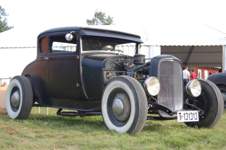 Black hot rod coupe with white wall tires and exposed engine. License plate reads T-131313