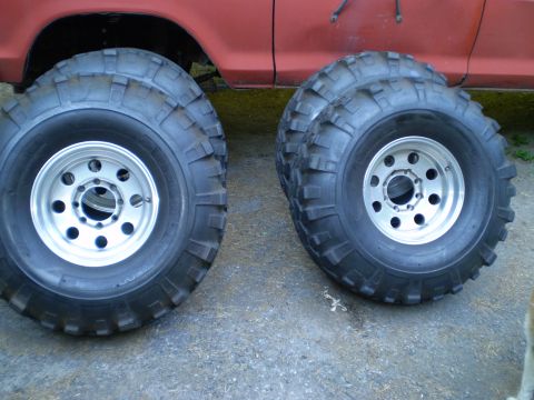 1979 Ford Bronco - Four off-road tires and wheels are displayed next to the red body of a vehicle.