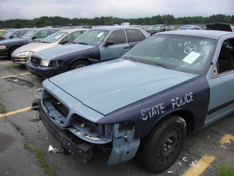2001 Ford Crown Victoria - A State Police car with front-end damage and "STATE POLICE" markings on the fender is parked in a lot with other vehicles.