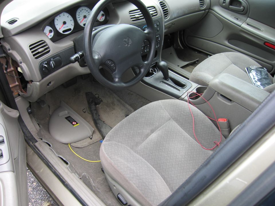 Car interior showing dashboard, steering wheel, seats, and center console. Some trim is removed on the left