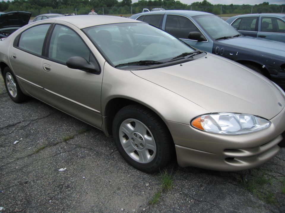 Gold sedan parked on cracked asphalt, front quarter view. Other cars are visible in the background