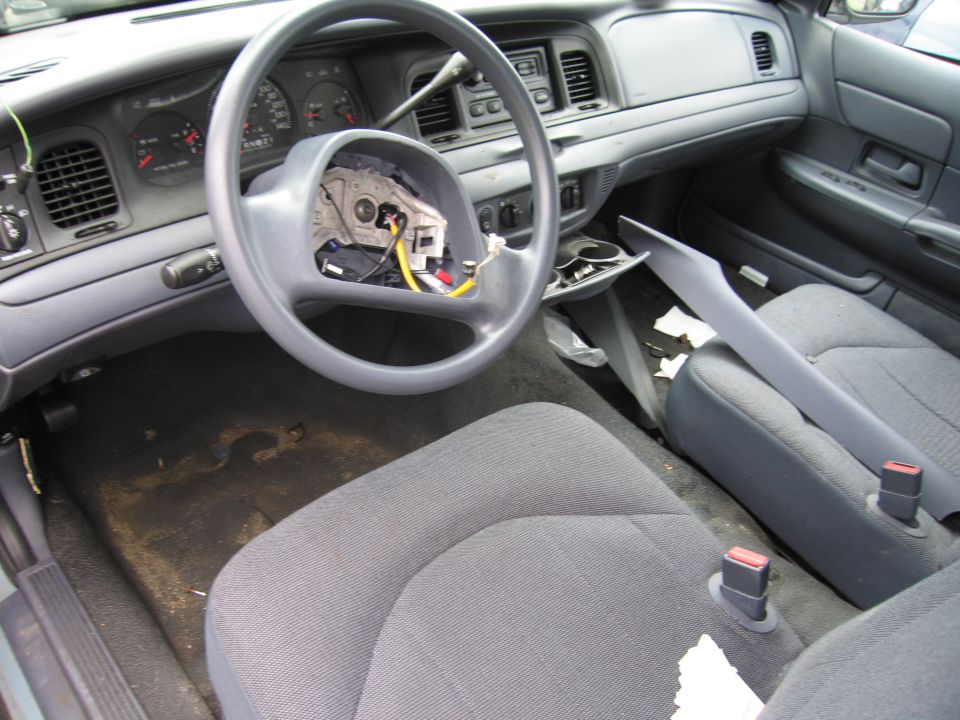 Interior of a 2001 Ford Crown Victoria, showing the dashboard, steering wheel, and seats. The steering wheel is partially disassembled