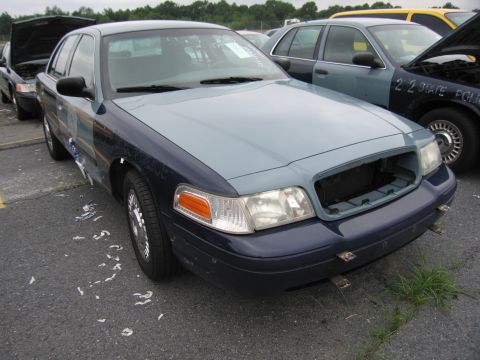 2001 Ford Crown Victoria - A damaged 2001 Ford Crown Victoria sits in a lot with other vehicles, one of which appears to be a police car.