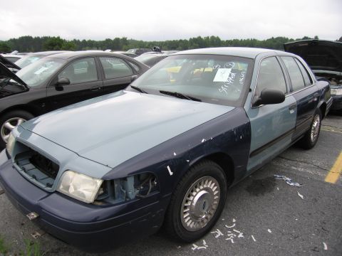 2001 Ford Crown Victoria - A two-tone 2001 Ford Crown Victoria is parked in a lot, showing damage to the front grille area.