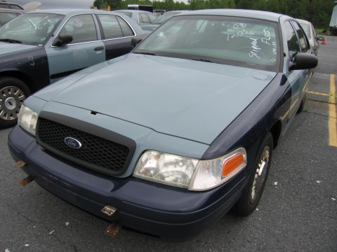 2001 Ford Crown Victoria - A two-tone blue 2001 Ford Crown Victoria is parked in a lot with other vehicles. White text on the windshield reads 'Stripped Floors'.
