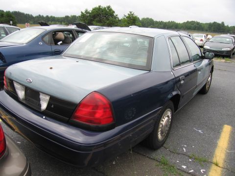 2001 Ford Crown Victoria - The rear of a two-tone Ford Crown Victoria is visible, parked in an outdoor lot with other vehicles.