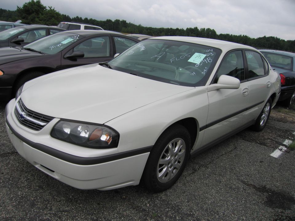 White sedan parked in lot, windshield has papers. Other cars visible
