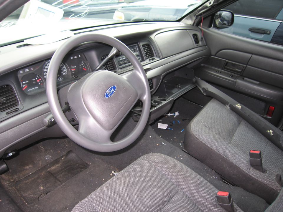 Interior of a 2001 Ford Crown Victoria showing the dashboard, steering wheel with Ford logo, and front seats. The interior appears dirty and somewhat dismantled