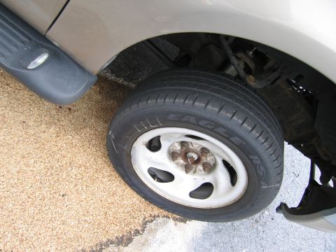 2001 Ford Crown Victoria - The front wheel and fender of a tan vehicle are visible, a black running board and a tire with 'EAGLE' branding.