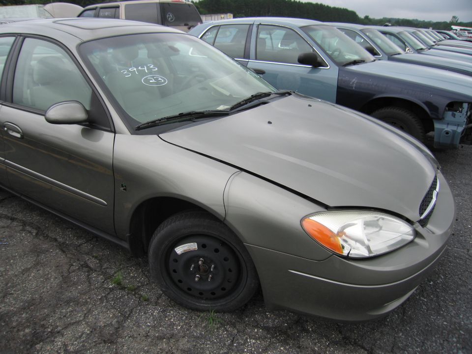 Gray Ford Taurus, front quarter view. Numbers 3943 and 23 written on windshield. Other cars in background
