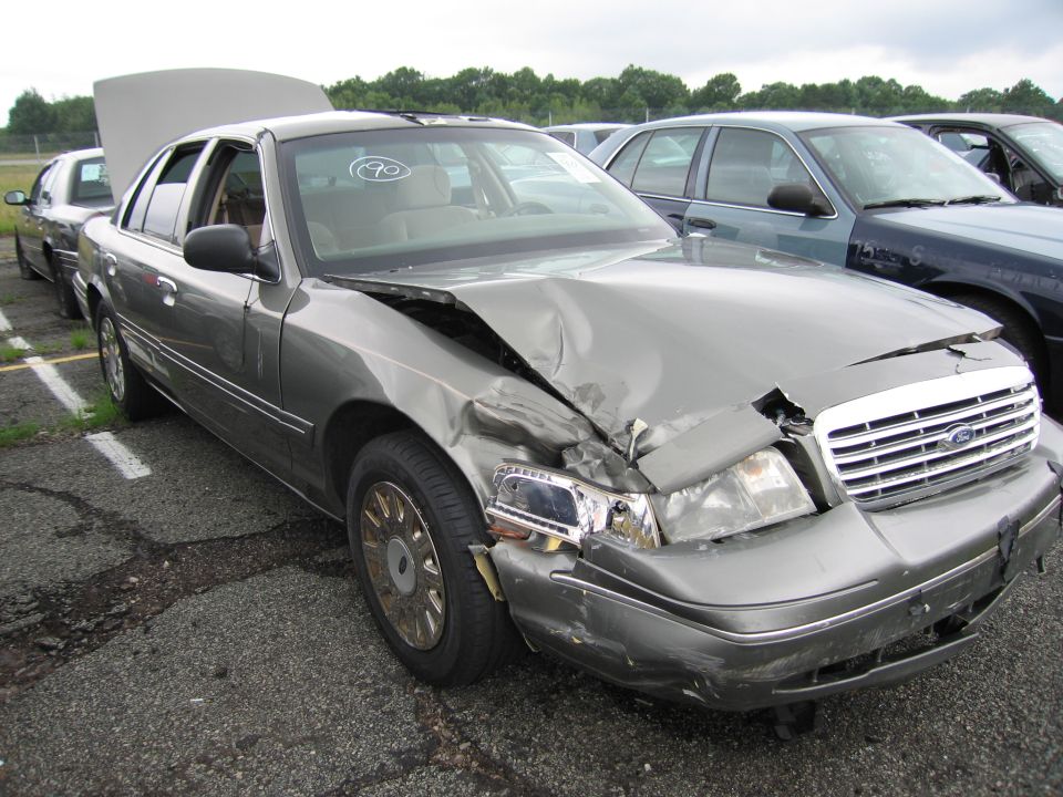Gray 2001 Ford Crown Victoria with extensive front-end damage, hood open, parked in a lot