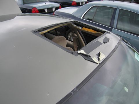 2001 Ford Crown Victoria - Interior view of a car with a damaged sunroof, showing the seats and roll cage. Other vehicles are parked in the background.